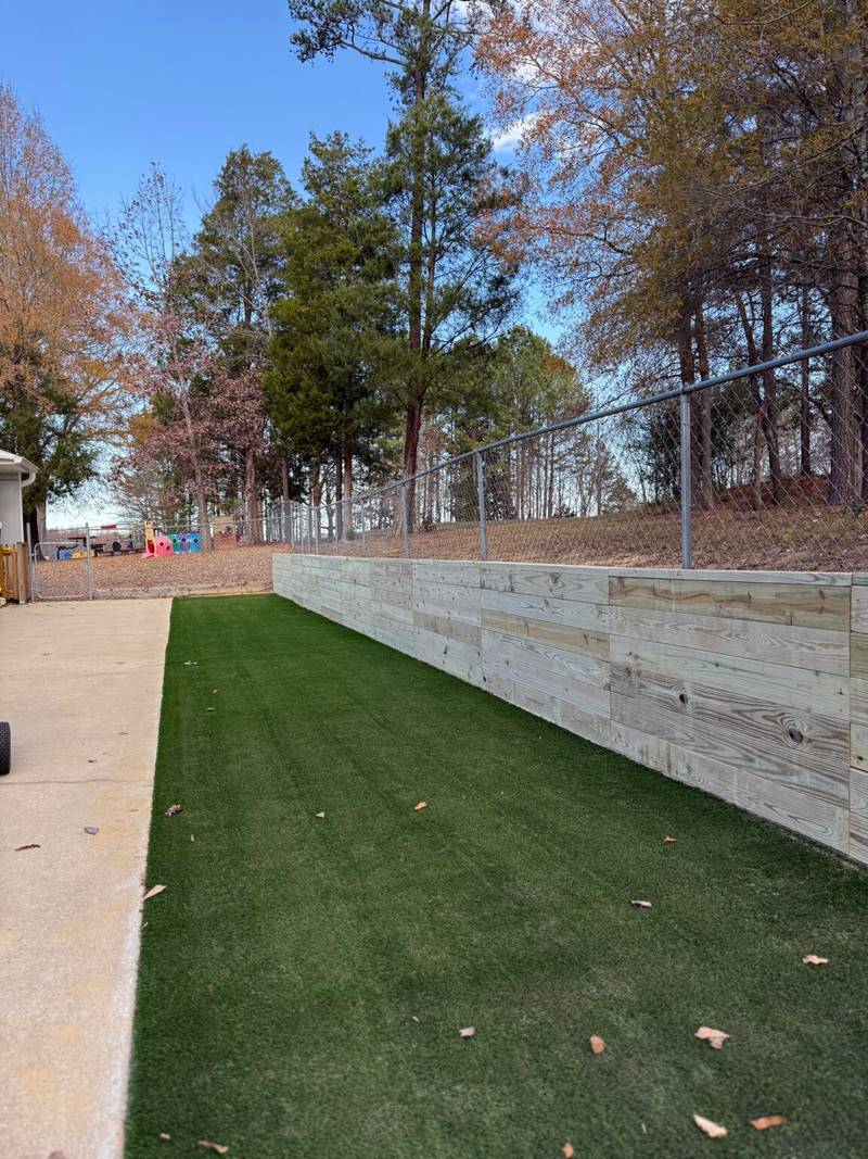 Finished Backyard Renewal with artificial turf, wooden retaining wall, and chain-link fence