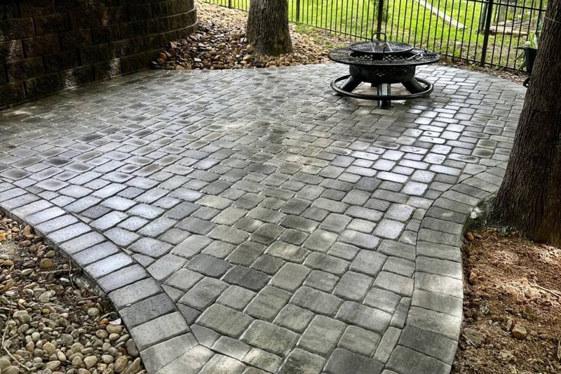 Backyard Escape - Project 1 Shaded Charlotte backyard with a gray paver patio, fire pit, trees, and block retaining wall